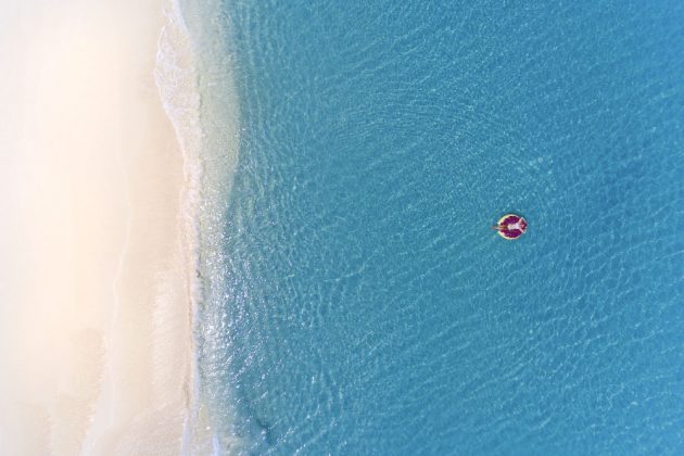 Aerial view of a woman floating in the clear waters just off a Cayman beach.